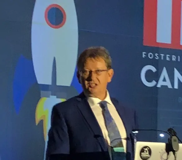 A man in a suit standing at a podium in front of a rocket.