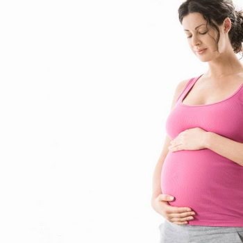 A pregnant woman in a pink tank top and gray pants gently holds her belly with both hands, reminiscent of the serene comfort found at a hot stone massage in Ottawa, standing gracefully against a white background.