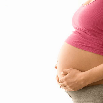 A person wearing a pink shirt and gray pants lovingly cradles their pregnant belly, reminiscent of the calm one might feel after a hot stone massage in Ottawa, all against a serene white backdrop.