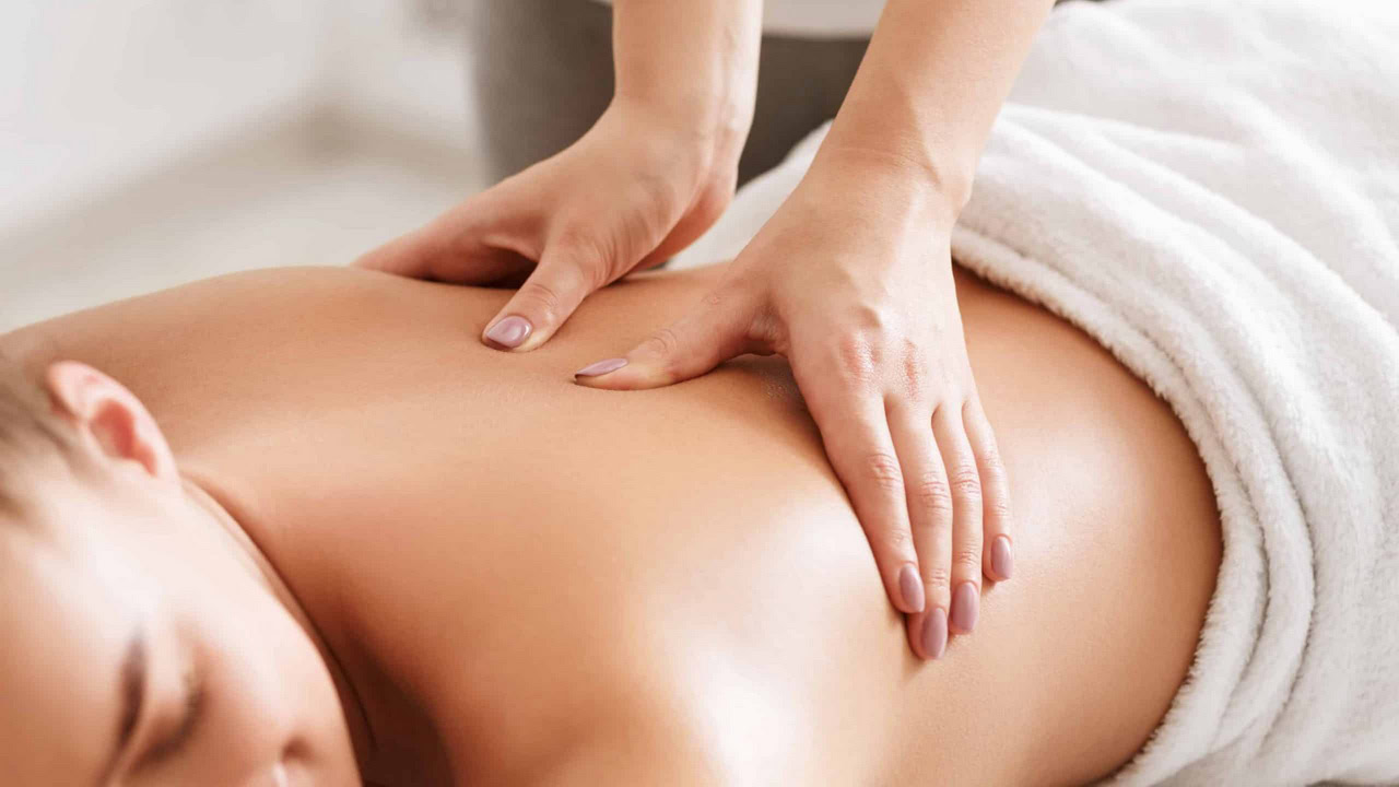 A person is receiving a deep-tissue massage, lying face down on a white towel, with skilled hands applying firm pressure.